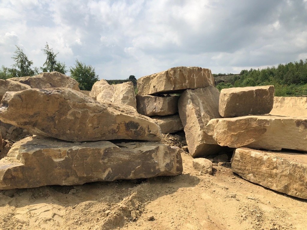 Large blocks of sandstone stacked at the quarry under a cloudy sky